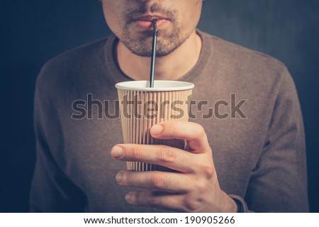 A young man is using a straw to drink from a paper cup