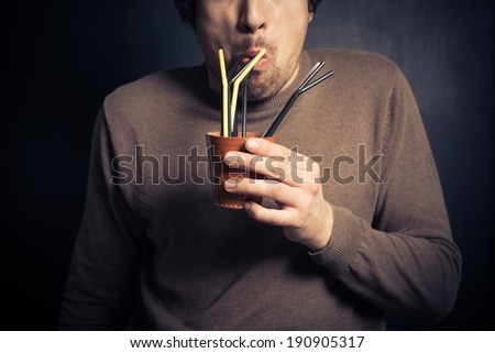 A silly young man is drinking from a leather cup with a bunch of colorful straws