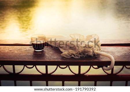 A glass of coffee and an umbrella on a wooden table by a lake in the afternoon