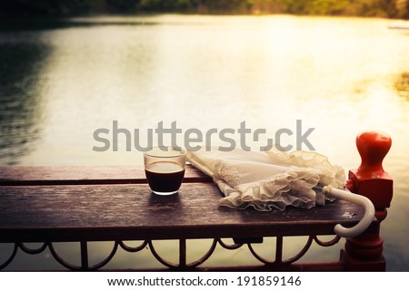 A glass of coffee and an umbrella on a wooden table by a lake in the afternoon