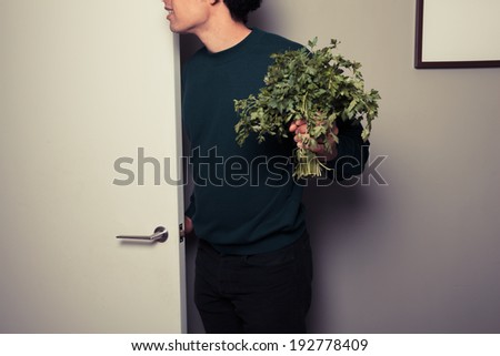 A young man with a big bunch of parsley in his hand is answering the door