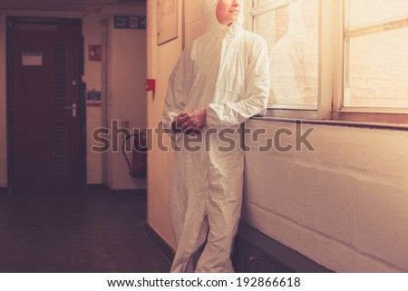 A scientist wearing a boiler suit is standing by  a window