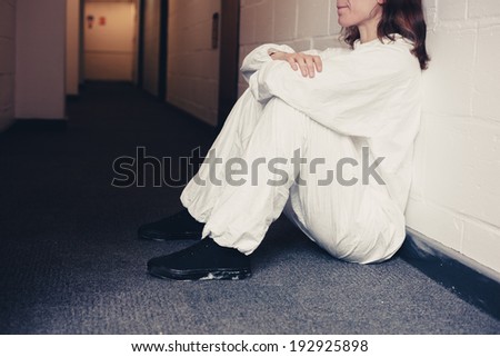 Young woman wearing a boiler suit is upset and is sitting in a corridor