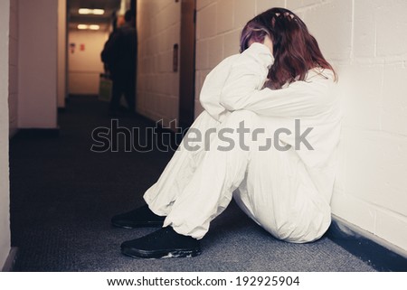 Young woman wearing a boiler suit is upset and is sitting in a corridor