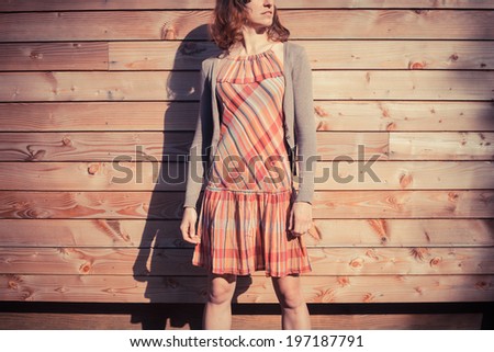 A young woman is posing outside a wooden cabin