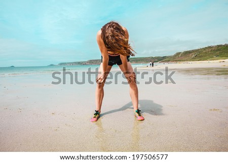An athletic young woman is exhausted after running on the beach
