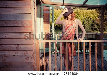 A young woman wearing a cowboy hat is standing on the porch of a cabin