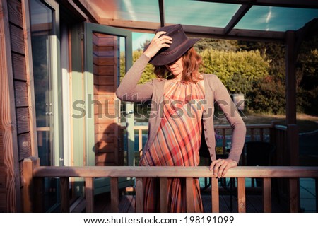 A young woman wearing a cowboy hat is standing on the porch of a cabin