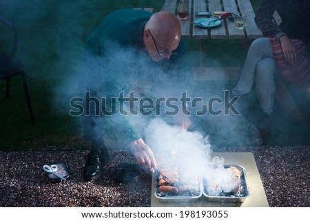 A senior man is cooking meat on a barbecue