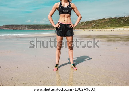 A fit young woman with toned abs is standing on the beach