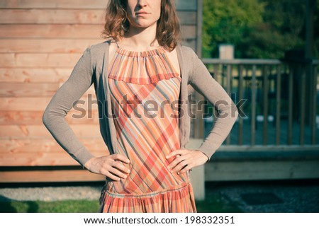 A young woman is standing by the porch of a wooden cabin