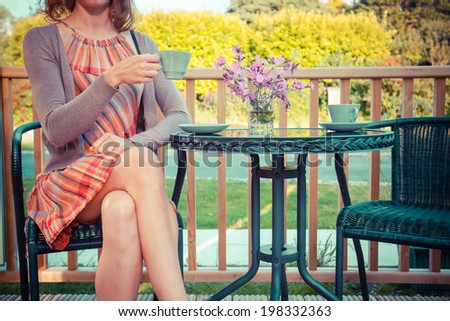 A young woman is sitting and drinking tea on the porch in summer