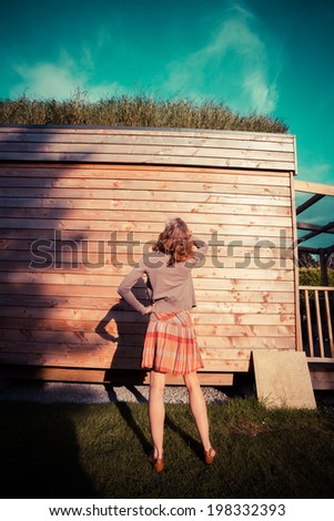 A young woman is standing in a garden outside a wooden cabin and is looking up