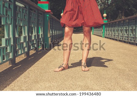 The legs of a young woman standing on a bridge in a park on a summer day