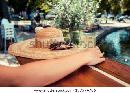 A young woman is drinking lemonade by a pond in the park