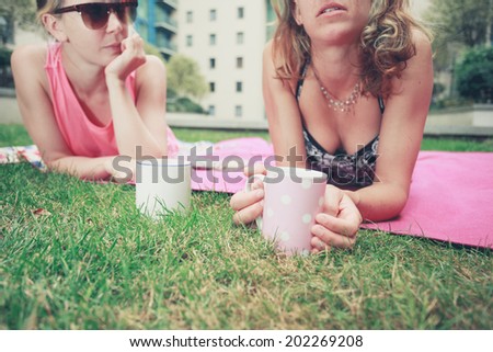 Two young women are having tea outside on the grass