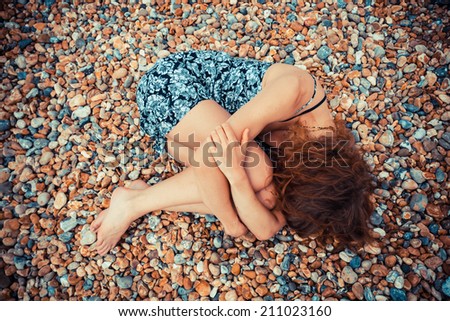 A young woman is lying curled up on a pebble beach
