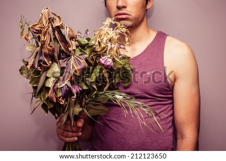 A sad young man is holding a bouquet of dead and withered flowers