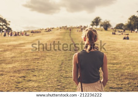 A young woman is walking up a hill in the park at sunset