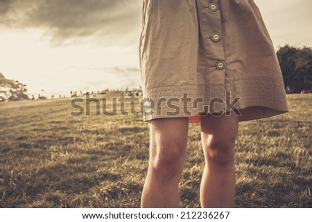 A young woman\'s skirt is blowing in the wind as she is standing in a park at sunset