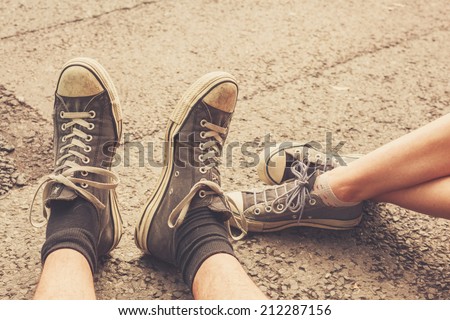 The feet of a young couple sitting in the street wearing similar shoes