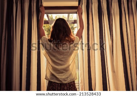 A young woman is opening the curtains at sunrise
