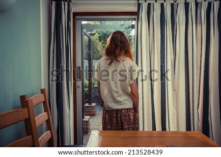 A young woman is standing by the curtains of a set of french doors