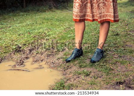 A young woman is standing by a puddle in the forest