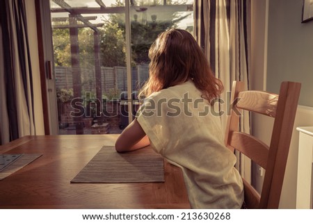 A young woman is sitting at a table at sunset and is looking out the window
