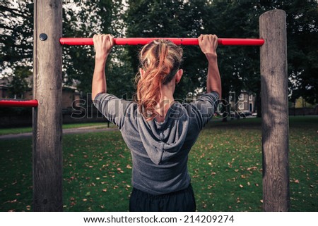 A young woman is doing pull ups in the park