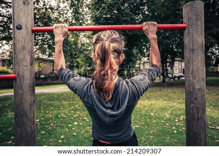 A young woman is doing pull ups in the park