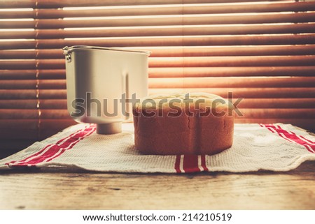 A freshly baked loaf of bread and a bread maker tin by the window bathed in sunlight