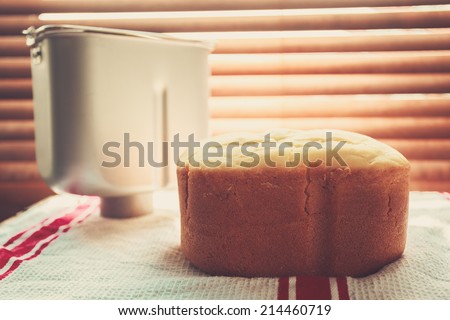 A freshly baked loaf of bread and a bread maker tin by the window bathed in sunlight