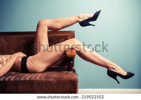 A sexy young woman wearing high heels is relaxing on a sofa in her underwear