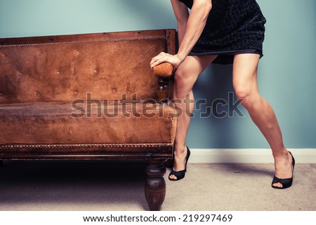 A sexy young woman in high heels is moving a sofa