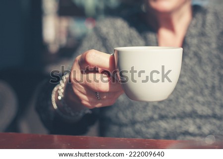 An elderly woman is having coffee outside in the street