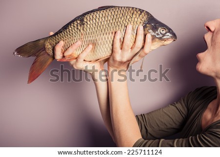 A young woman is posing with carp and is pulling silly faces