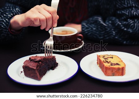A young woman is having coffee and two different types of cake