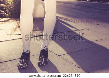 The legs of a young woman standing in the street on a sunny day