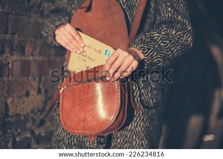 A young woman is getting a letter out of her bag at sunset as she is walking in the street