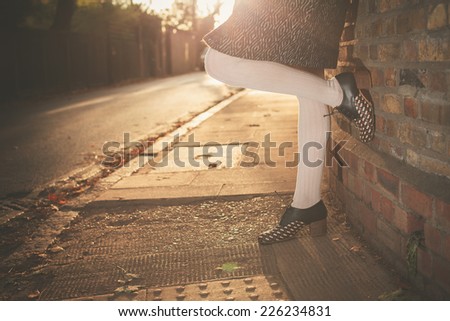 The legs of a young woman resting up against a wall at sunset on an autumn day