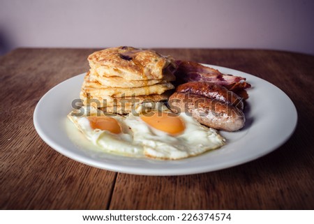 A breakfast with short stack of pancakes, bacon, eggs and sausage