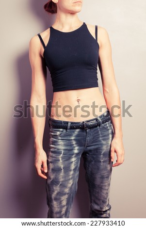 A young woman with toned abs is posing in front of a purple wall