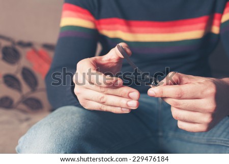 A young man is sitting on a sofa and is clipping his finger nails