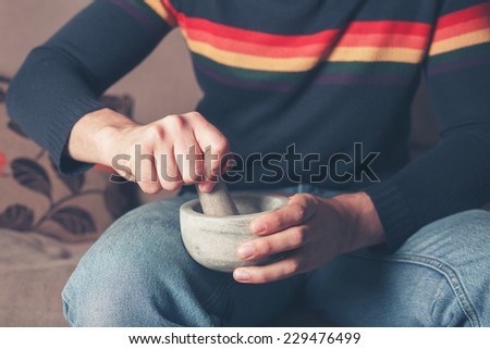 A young man is sitting on a sofa and is grinding pepper with a pestle and mortar