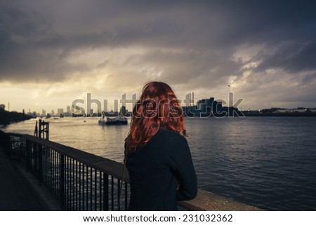 A young woman is admiring the sunset over a river in the city on a cold autumn day