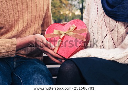 A young man is giving a woman a heart shaped box in the park