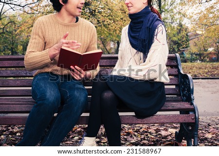 A young man is reading to a young woman on a park bench in autumn