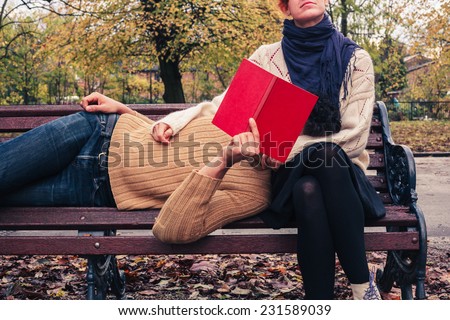 A young couple is reading and relaxing on a park bench in autumn