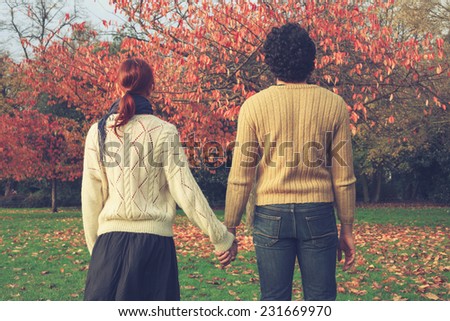 A young couple is holding hands in the park by a tree in autumn